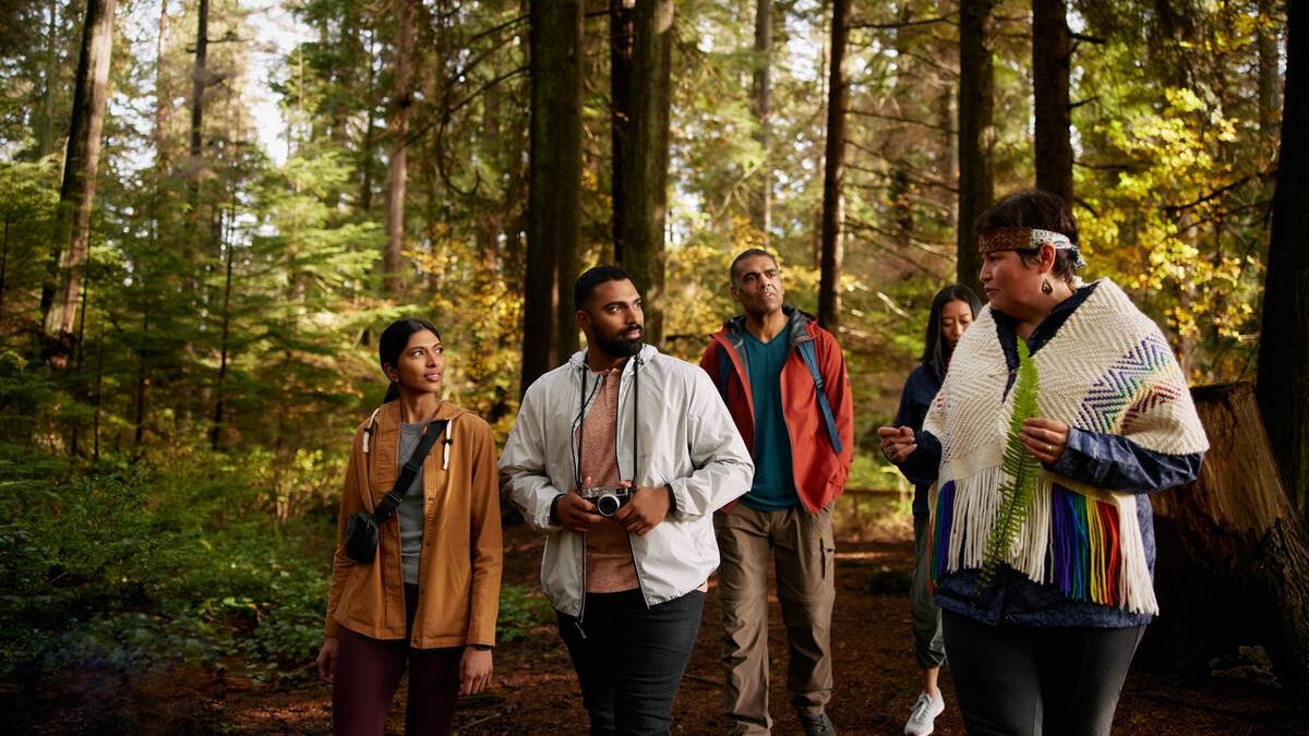 Candace Campo from Talaysay Walking Indigenous Tours is conducting a presentation and speaking to a group while on a walking experience in Stanley Park in Vancouver.
